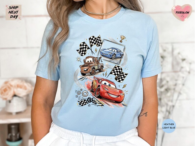 A woman wearing a light blue t-shirt with a graphic of three cartoon cars racing, including a red car, a blue car, and a brown truck.
