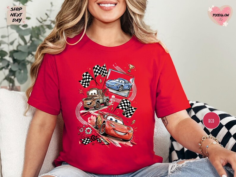 A woman wearing a red t-shirt with a graphic of three animated cars racing, including a blue car, a red car, and a brown truck, along with checkered flags and other racing elements.