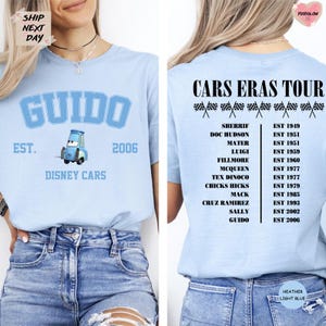 a woman wearing a light blue t-shirt with a graphic of a blue car and text related to a Cars Eras Tour.