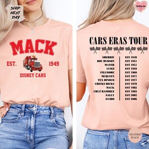 a woman wearing a pink t-shirt with the text "MACK EST. 1949 DISNEY CARS" printed on it. The t-shirt also has a list of Disney car owners, including Sherif, Doc Doon, Mater, Luigi, Mcqueen, Tex Dino, Chick's Mack, Cruz Ramiz, Sally, Guido, and Heather Peach.