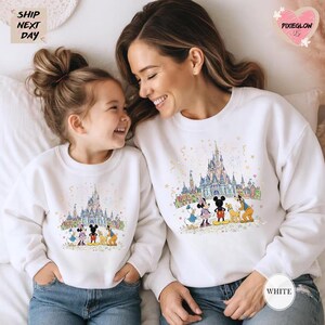 A smiling woman and a young girl wearing matching Disney-themed sweatshirts with Mickey Mouse and Minnie Mouse illustrations.