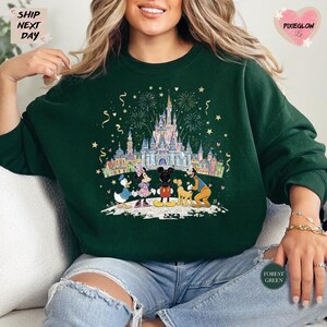 A woman wearing a green sweatshirt with a colorful illustration of Disney characters and a castle, surrounded by fireworks.
