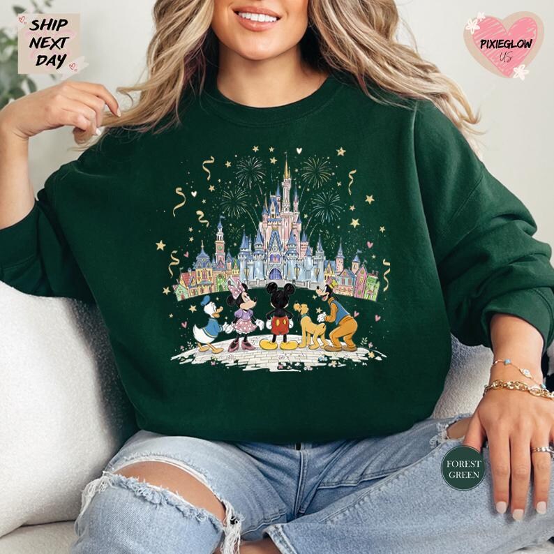 A woman wearing a green sweatshirt with a colorful illustration of Disney characters and a castle, surrounded by fireworks.