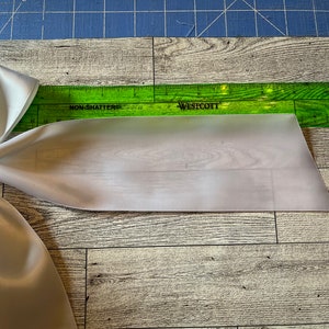 May include: A white satin ribbon bow with a green ruler measuring 30.5 cm. The ruler is labelled "Westcott" and "Non-Shatter".
