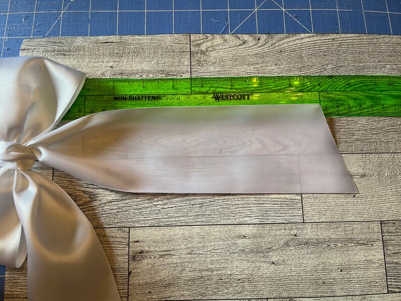 May include: A white satin ribbon bow with a green ruler measuring 30.5 cm. The ruler is labelled "Westcott" and "Non-Shatter".