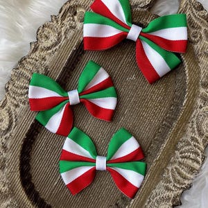 May include: Three red, white and green bow hair clips. The bows are made of ribbon and have a white centre.