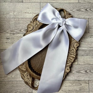 May include: A white satin ribbon tied into a large bow, displayed on a wooden serving tray with a decorative carved edge.