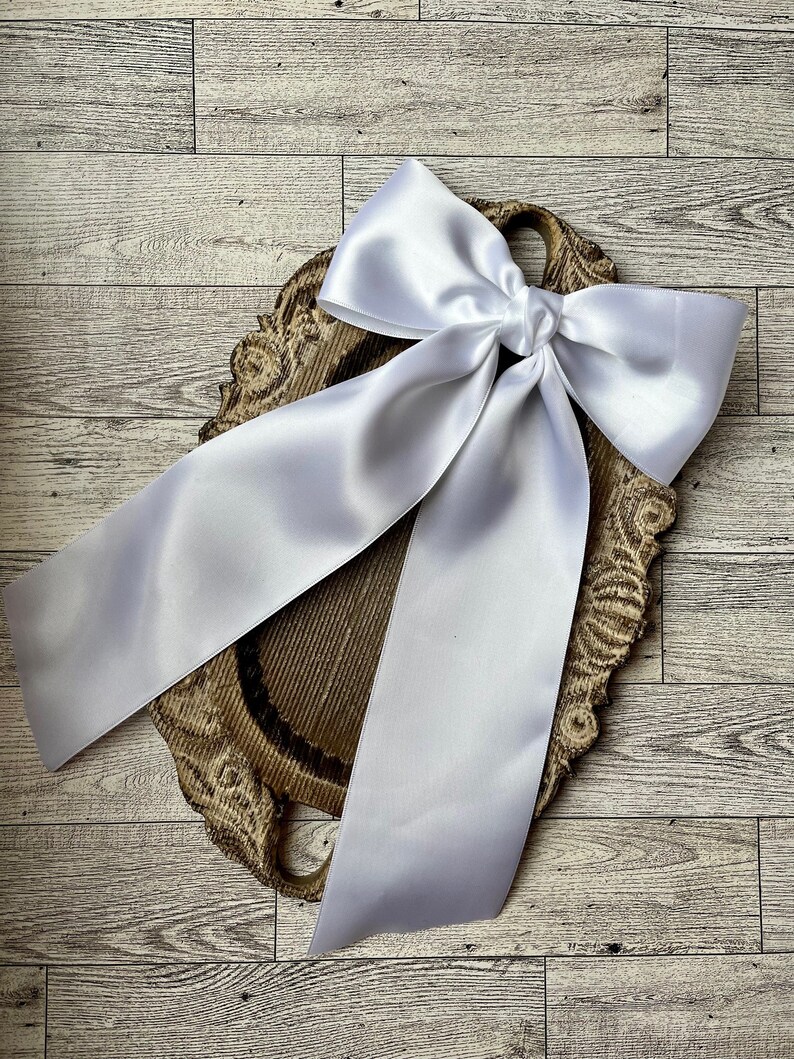 May include: A white satin ribbon tied into a large bow, displayed on a wooden serving tray with a decorative carved edge.