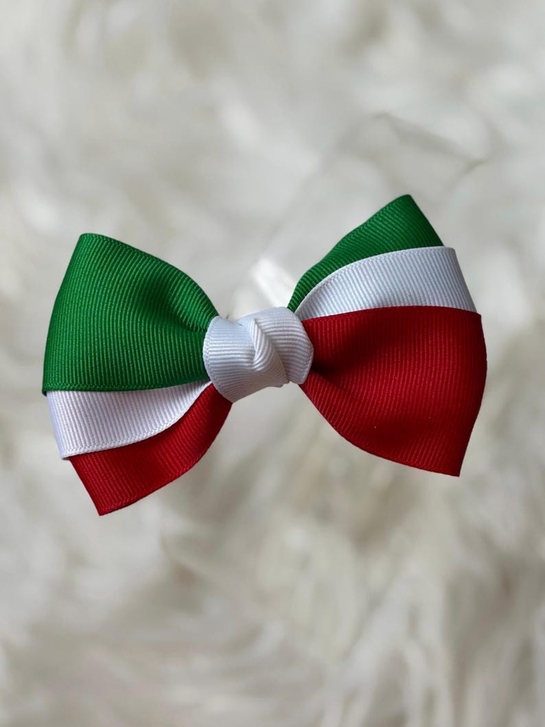 May include: A handmade bow featuring the colors of the Italian flag: green, white, and red. The bow is made of grosgrain ribbon and has a knot in the center. The bow is likely for hair accessories or decorative purposes.