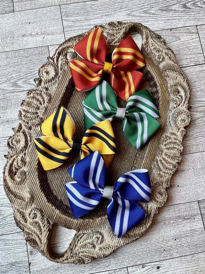 May include: Four hair bows with striped patterns in the colors of the Hogwarts houses: Gryffindor (red and gold), Slytherin (green and silver), Hufflepuff (yellow and black), and Ravenclaw (blue and bronze).