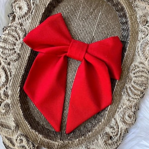 Puede incluir: Un gran lazo rojo brillante hecho de tela. El lazo está sentado en una bandeja decorativa, adornada y dorada.