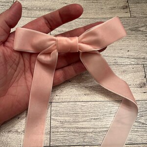 May include: A blush pink satin ribbon tied into a bow. The ribbon is long enough to tie around a gift or use for other craft projects.