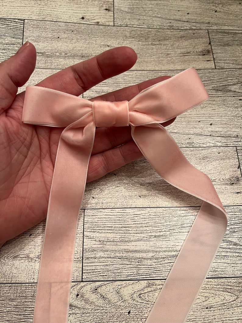 May include: A blush pink satin ribbon tied into a bow. The ribbon is long enough to tie around a gift or use for other craft projects.