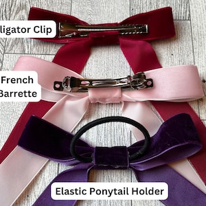 May include: Three velvet ribbon hair bows with different fasteners: an alligator clip, a French barrette, and an elastic ponytail holder. The bows are in burgundy, pink, and purple.