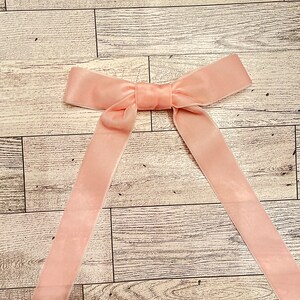 May include: A blush pink velvet ribbon bow with long tails. The bow is tied and ready to be used for a gift or craft project.