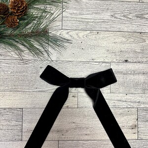 May include: A black velvet bow tie on a white wood background.