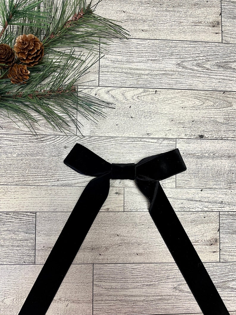 May include: A black velvet bow tie on a white wood background.