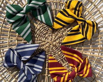 May include: Four fabric hair bows featuring striped patterns in distinct color combinations: green and silver, yellow and black, navy blue and silver, and maroon and gold. Each bow is constructed with multiple folded loops and pointed ends.
