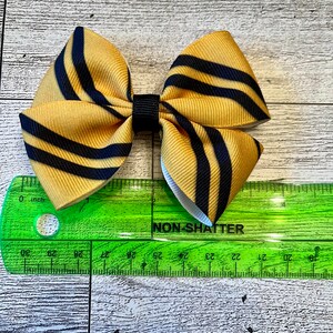 May include: A yellow and black striped bow with a black center. The bow is approximately 2 inches wide.