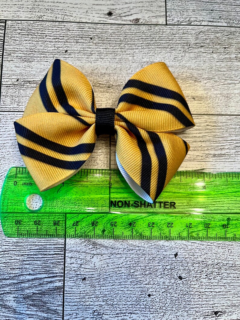 May include: A yellow and black striped bow with a black center. The bow is approximately 2 inches wide.