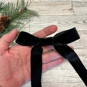 May include: A black velvet bow with long tails. The bow is tied in a classic shape and is perfect for adding a touch of elegance to any gift or occasion.