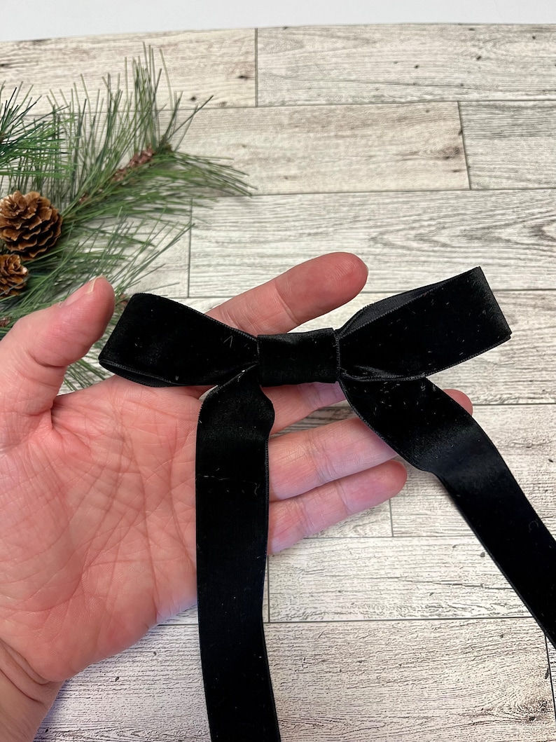 May include: A black velvet bow with long tails. The bow is tied in a classic shape and is perfect for adding a touch of elegance to any gift or occasion.