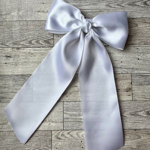 May include: A large white satin bow with long tails. The bow is tied in a knot and the tails are hanging down.