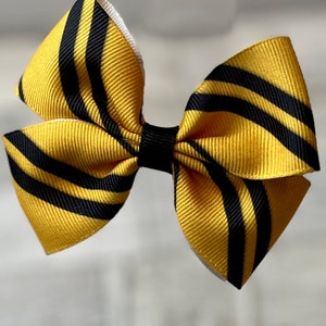 May include: A yellow and black striped hair bow. The bow is made of ribbon and has a white backing.