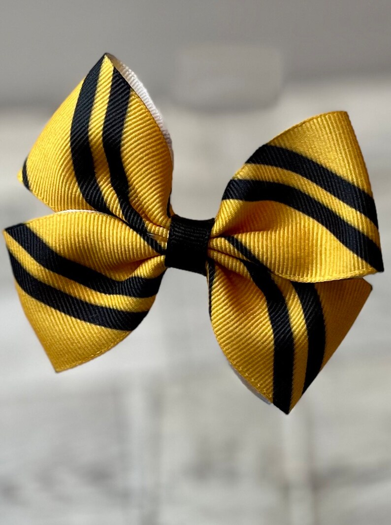 May include: A yellow and black striped hair bow. The bow is made of ribbon and has a white backing.