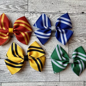 May include: Four handmade hair bows in different color combinations. The bows are made of striped fabric and are tied with a white ribbon. The bows are arranged on a light wood background.