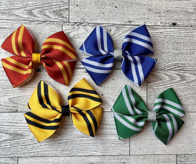May include: Four handmade hair bows in different color combinations. The bows are made of striped fabric and are tied with a white ribbon. The bows are arranged on a light wood background.