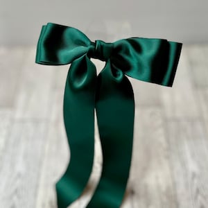 May include: A large, dark green satin bow with long tails. The bow is tied in a classic style and is perfect for adding a touch of elegance to any occasion.