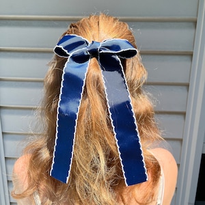 May include: A navy blue ribbon with white scalloped edges tied into a bow in someone's hair.