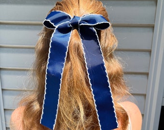 May include: A navy blue ribbon with white scalloped edges tied into a bow in someone's hair.