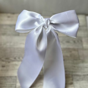 May include: A white satin ribbon tied into a large bow with long tails.
