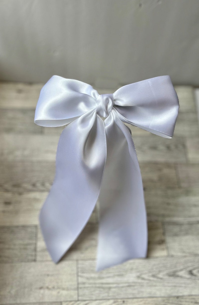 May include: A white satin ribbon tied into a large bow with long tails.