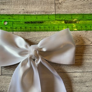 May include: A large white satin bow with a long tail. The bow is approximately 15 cm wide and 25 cm long.