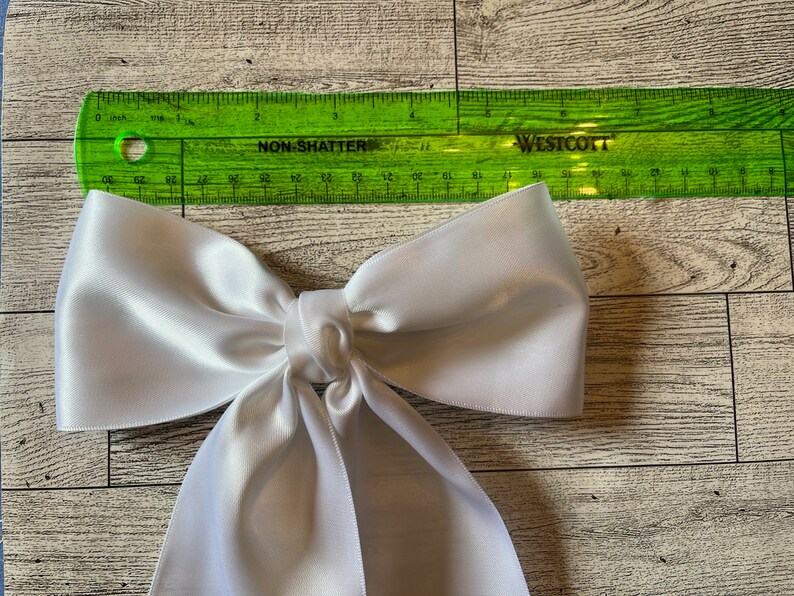 May include: A large white satin bow with a long tail. The bow is approximately 15 cm wide and 25 cm long.