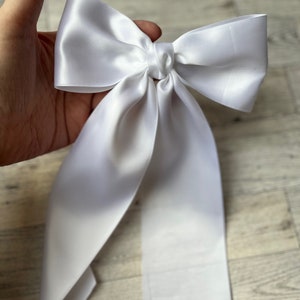 May include: A white satin bow with long tails. The bow is tied in a knot and the tails are flowing.