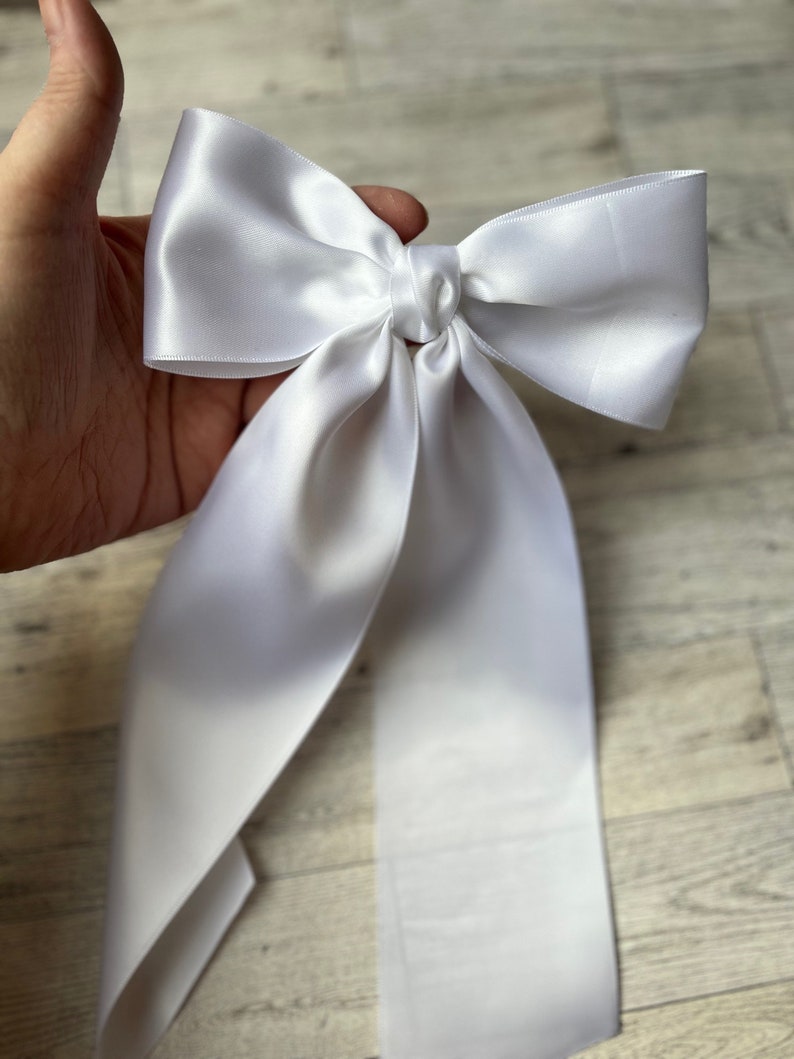 May include: A white satin bow with long tails. The bow is tied in a knot and the tails are flowing.