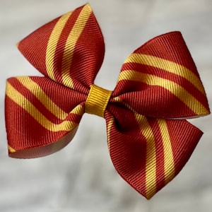 May include: A red and gold striped hair bow. The bow is made of ribbon and has a gold center.
