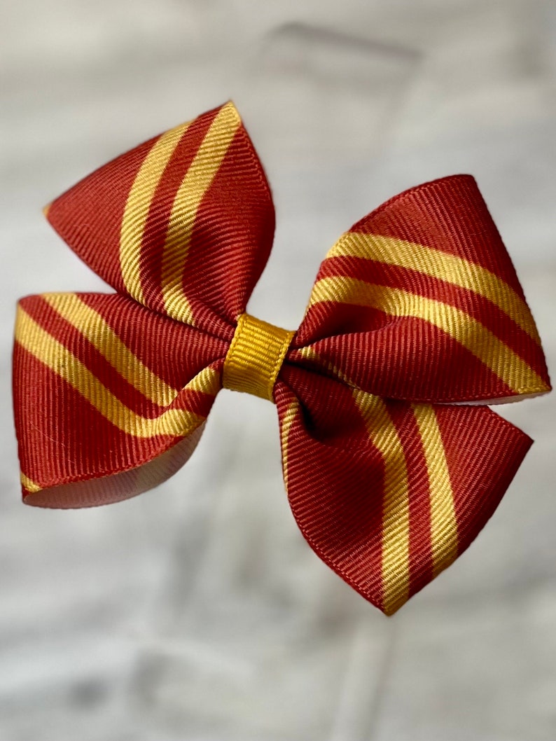 May include: A red and gold striped hair bow. The bow is made of ribbon and has a gold center.
