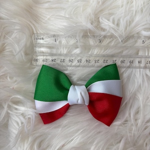May include: A handmade bow featuring the colors of the Italian flag: green, white, and red. The bow is made of grosgrain ribbon and measures approximately 4 inches in length. The bow is centered with a white knot.
