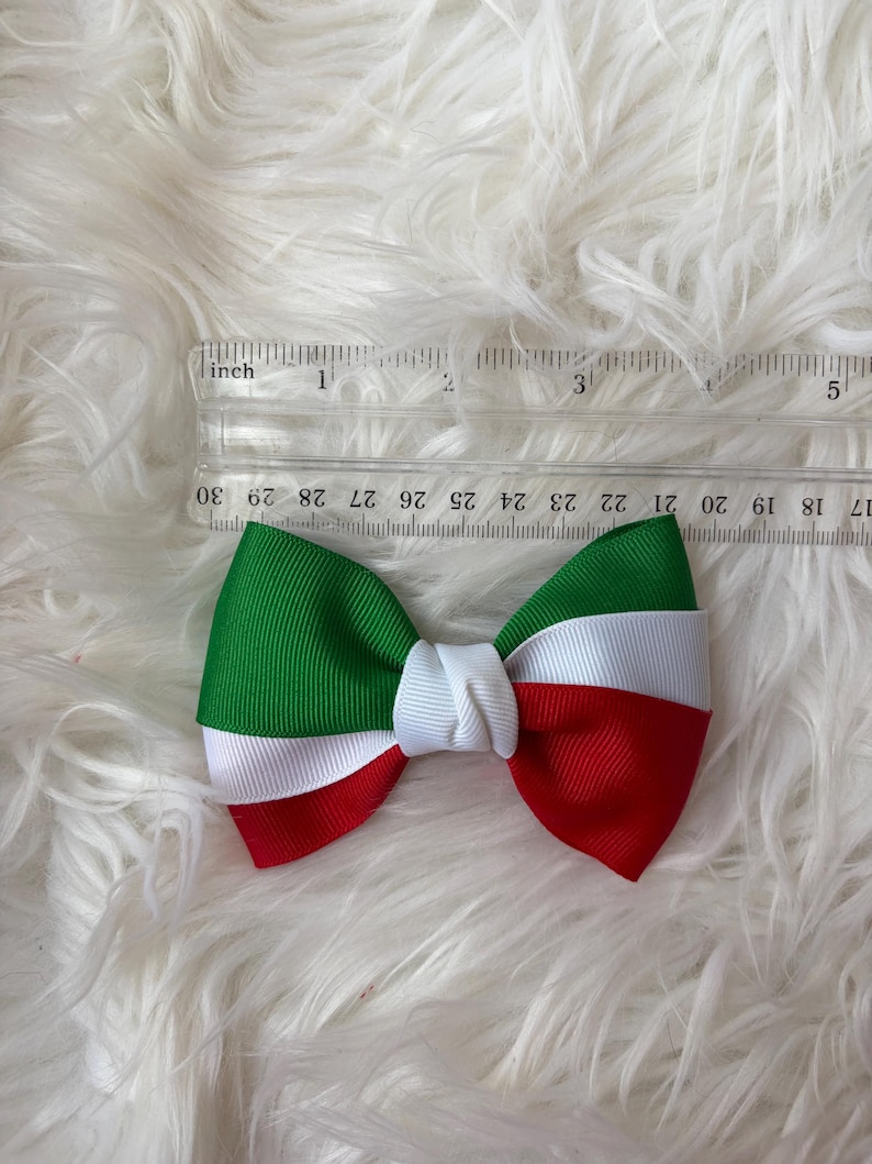 May include: A handmade bow featuring the colors of the Italian flag: green, white, and red. The bow is made of grosgrain ribbon and measures approximately 4 inches in length. The bow is centered with a white knot.