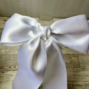 May include: A large white satin bow with long tails. The bow is tied with a knot in the centre.