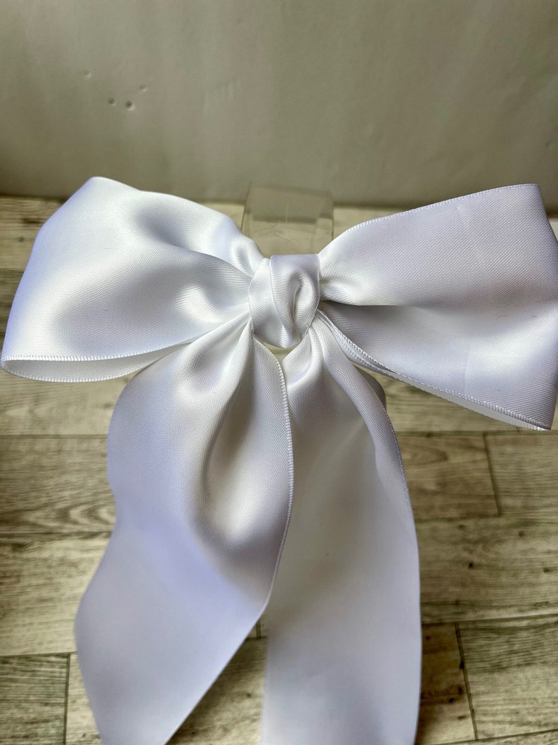 May include: A large white satin bow with long tails. The bow is tied with a knot in the centre.