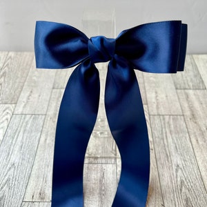 Puede incluir: Un lazo de cinta de satén azul marino con colas largas. El lazo está atado en un estilo clásico y es perfecto para agregar un toque de elegancia a cualquier ocasión.
