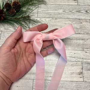 May include: A pink velvet ribbon bow with long tails. The bow is tied in a simple knot and the tails are straight.