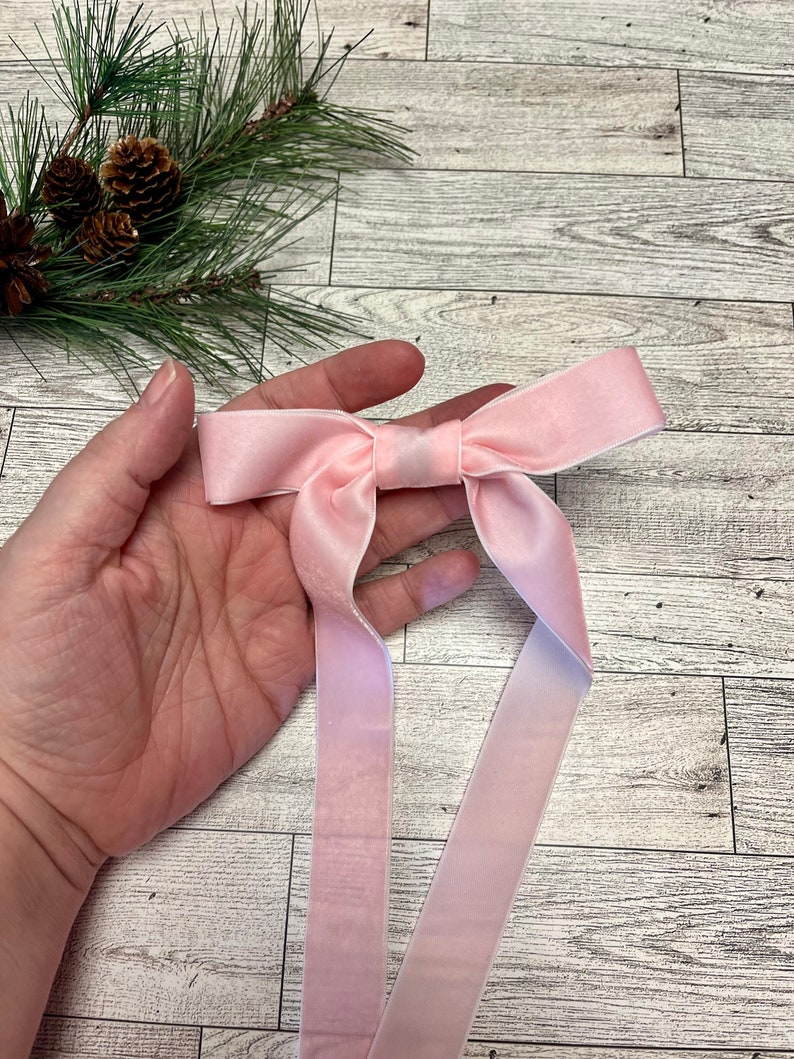 May include: A pink velvet ribbon bow with long tails. The bow is tied in a simple knot and the tails are straight.