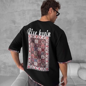 May include: Black short-sleeved t-shirt with a colourful patterned rug design and the text "Rise kyrin" printed on the back.